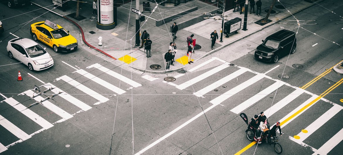 Vista aérea de un paso de peatones en San Francisco, con gente esperando en la esquina y vehículos en la calle.