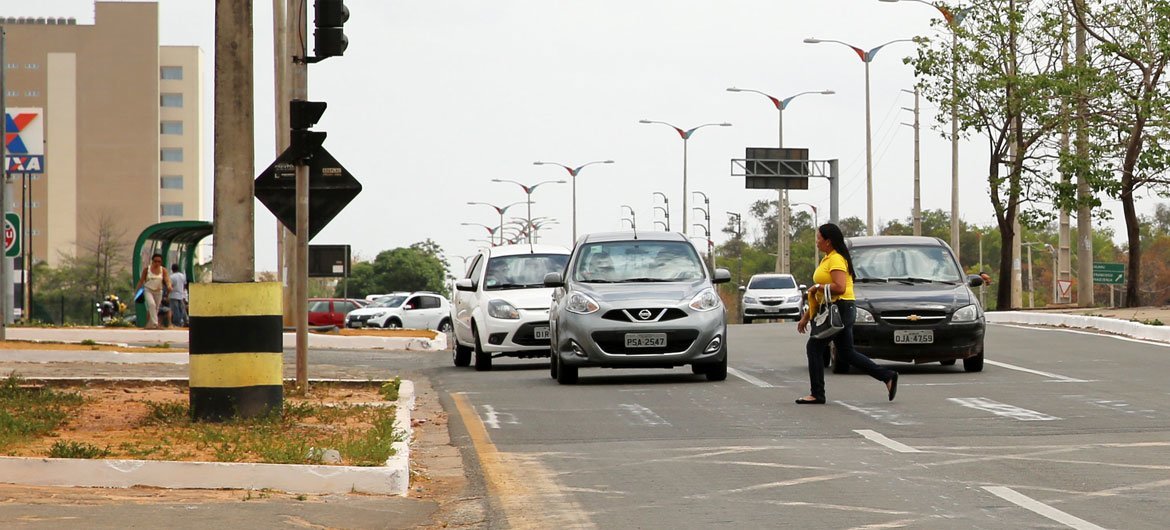 Una mujer con una camisa amarilla cruza una carretera de varios carriles en Brasil, con varios coches detenidos en el tráfico detrás de ella.