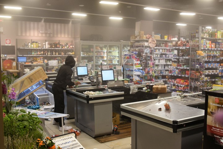 Un encapuchado permanece de pie cerca de una caja registradora dentro de un supermercado dañado durante las protetas en Milán. Foto Reuters /Stringer